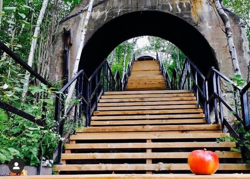 Un escalier monte dans des arches formées par d'anciennes conduites d'eau forcées. Au bas de l'escalier, on voit une pomme rouge.